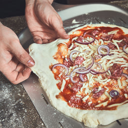 946052 Belegde pizza wordt uitgespreid op de 14-inch pizzabodem