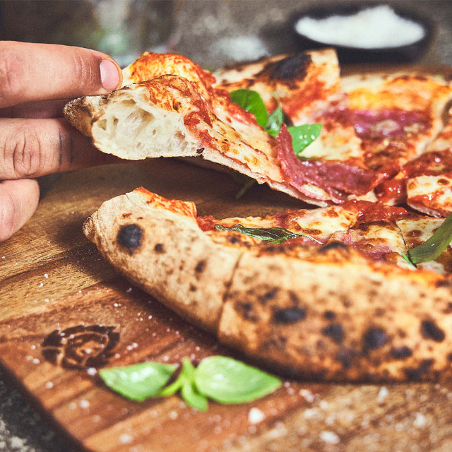 Afgewerkte pizza wordt van de acaciahouten pizzaplaat gehaald