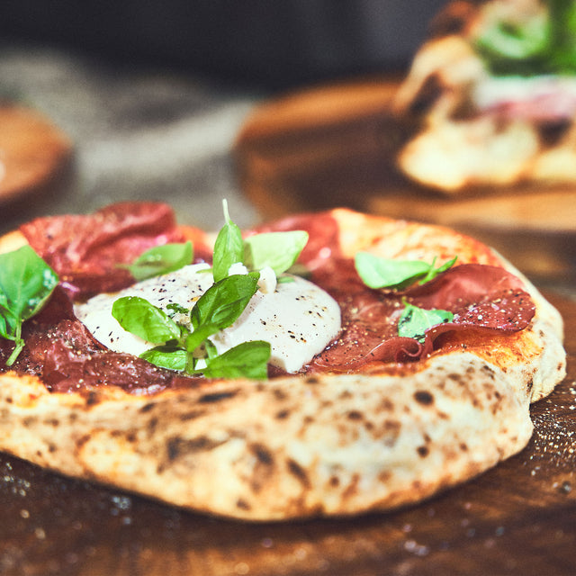 Kant-en-klare Napolitaanse pizza met een luchtige korst, belegd met burrata, salami en basilicum